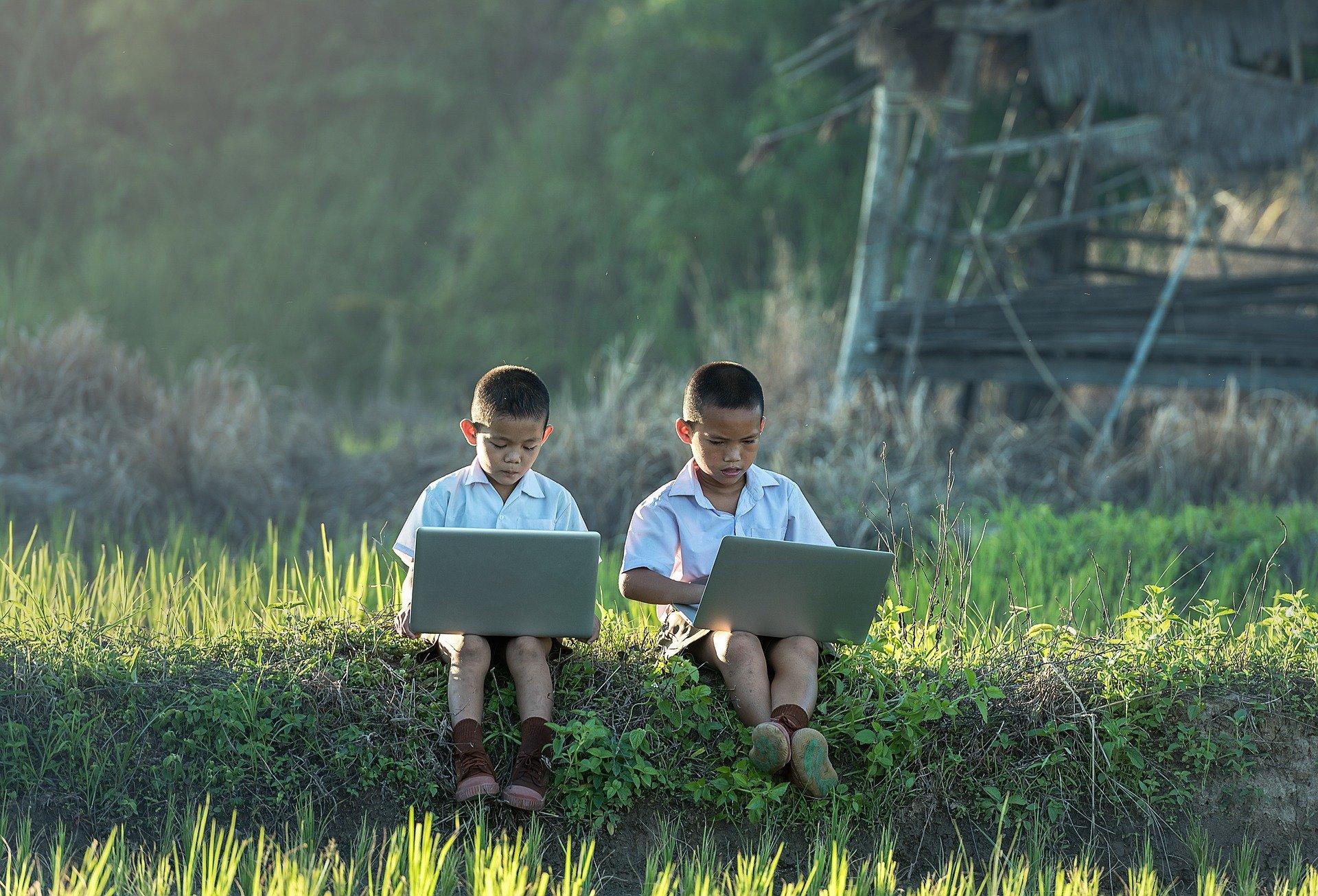 niños asiáticos sentados en un prado con un ordenador portátil