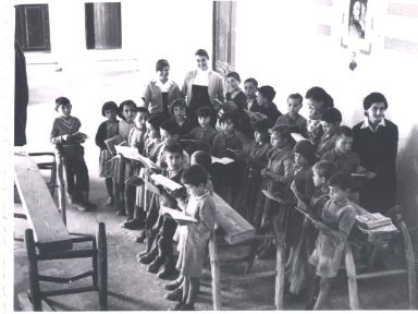 Niños leyendo en una clase antigüa con sus maestras