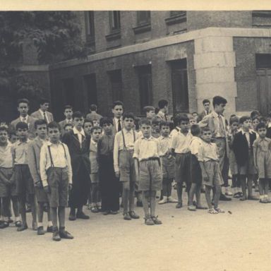 Fotografía antigüa de niños ordenados en fila junto a sus maestros