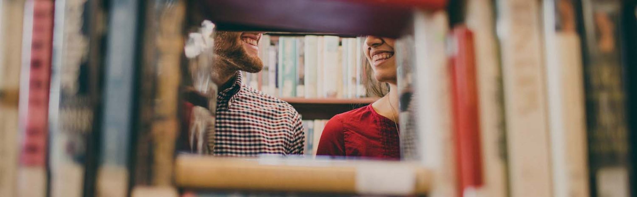 Chica y chico miran a través del hueco que dejan los libros en una estantería.