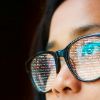 Chica mirando una pantalla con un código que se refleja en el cristal de sus gafas.